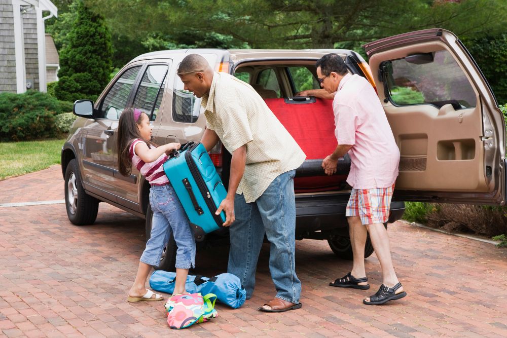 Two adults and a child pack colorful luggage into the back of a station wagon.